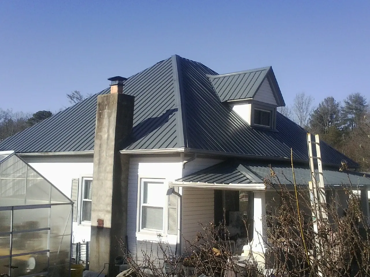 Dark blue standing seam metal roof on a white farmhouse with dormer — Slate & Tile Roof Repair by Roofing Brothers in New Brunswick