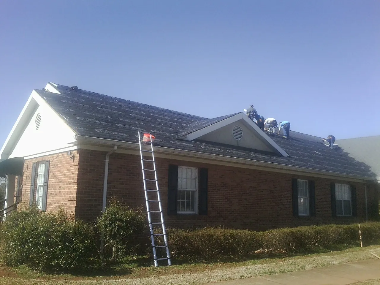 Crew tearing shingles off a brick ranch roof with a ladder set — Metal Roof Repair work by our crew in New Brunswick
