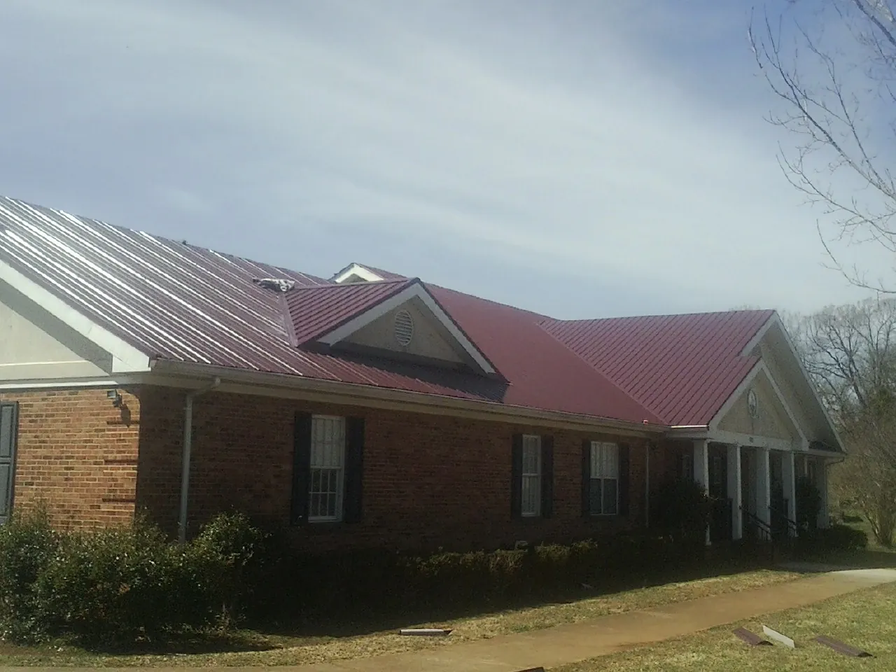 Red metal roof with gabled entries on a long brick building, from a Hail Damage Roof Repair job in New Brunswick