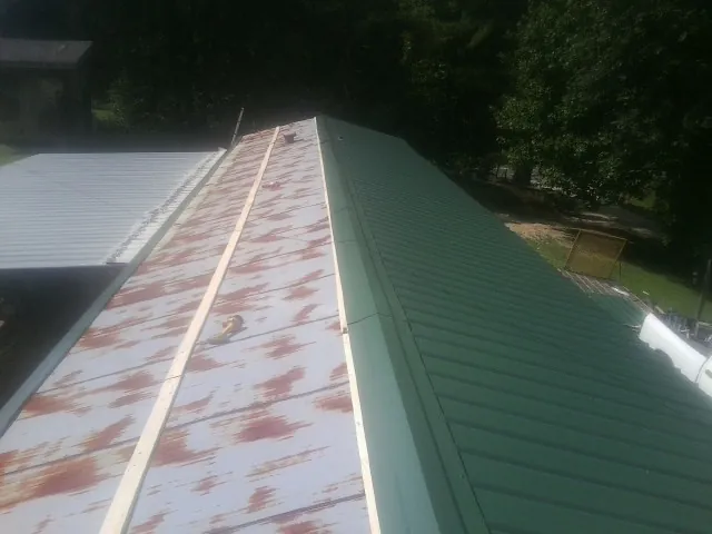 Old rusted panels beside newly installed green metal roofing in New Brunswick