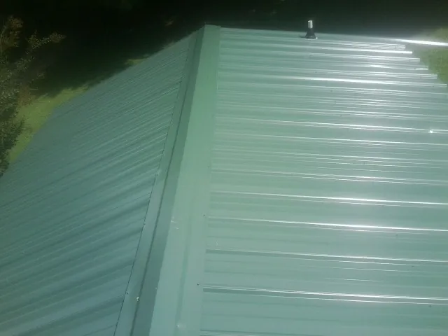 New green metal panels meeting at the ridge of a roof — Flat Roof Repair work by our crew in New Brunswick