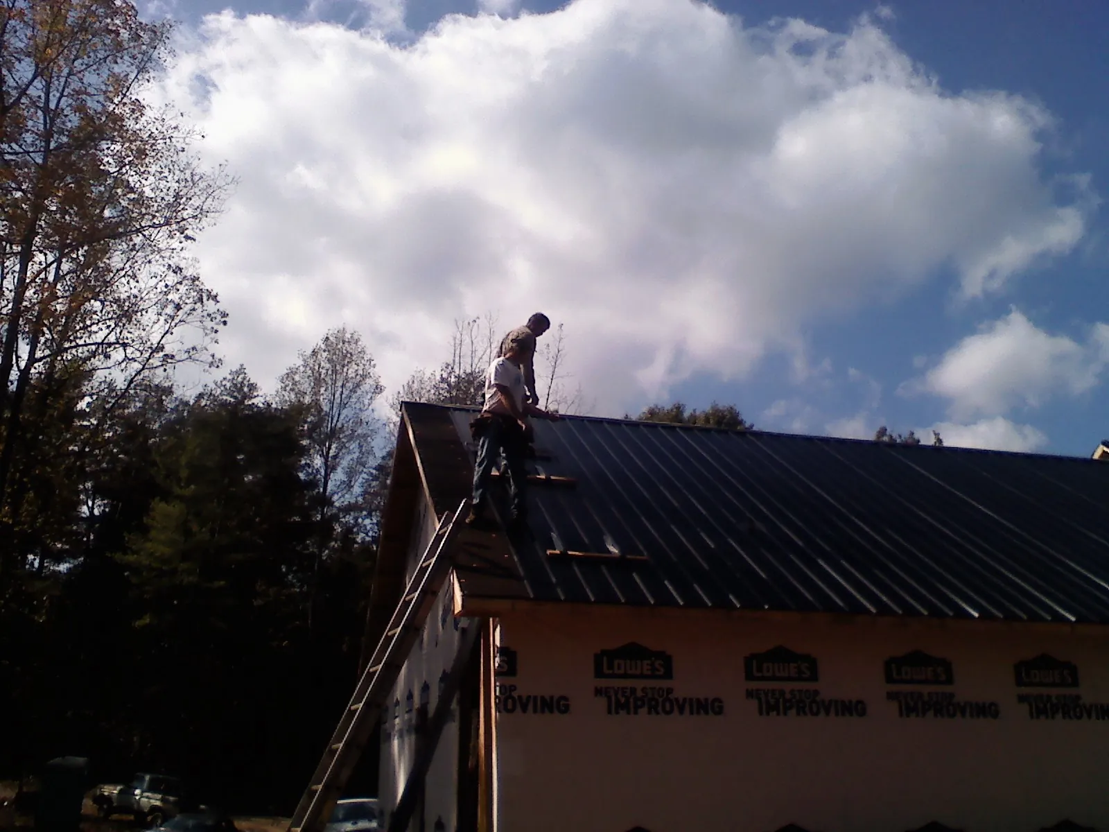 Roofer fastening dark metal panels high against a cloudy sky, from a Roof Inspection job in New Brunswick