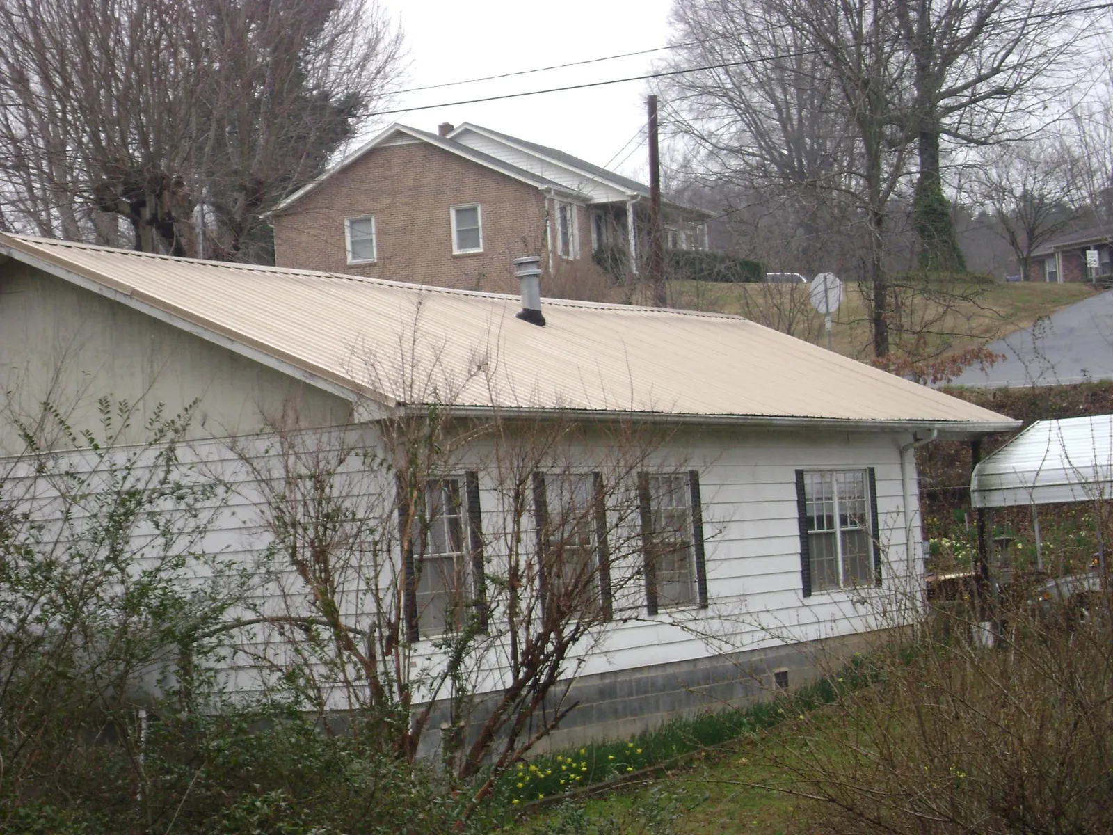 Tan metal roof on a white sided house set into a hillside — Commercial Roofing by Roofing Brothers in New Brunswick