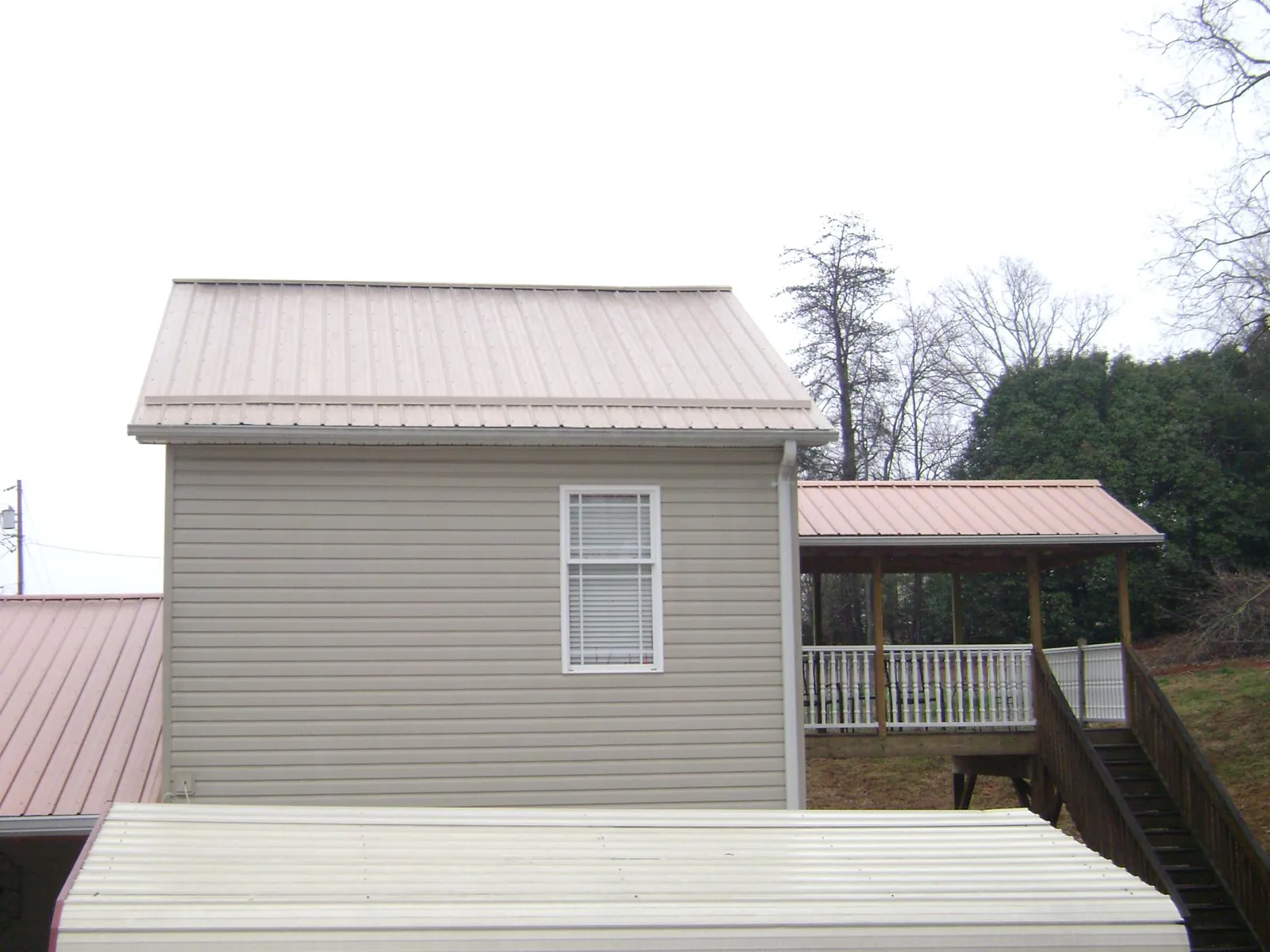Tan metal roofs on a two story addition and attached porch, from a Roof Replacement job in New Brunswick